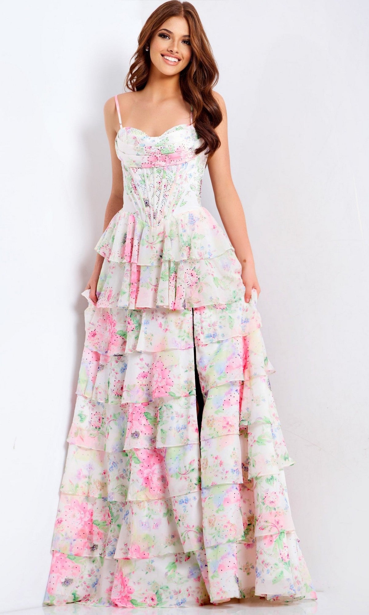 A woman poses against a white background in the Jovani 47282 long prom dress featuring pastel floral print, spaghetti straps, a fitted corset bodice, and a tiered skirt.